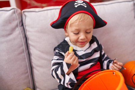 Foto de Adorable chico caucásico con traje de pirata comiendo dulce en casa - Imagen libre de derechos