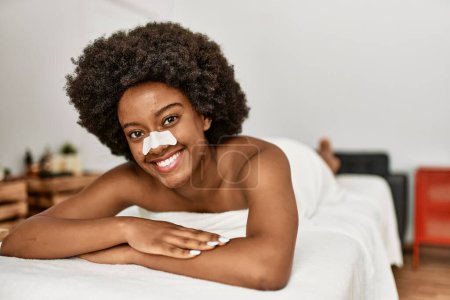 Foto de Mujer afroamericana joven sonriendo confiada usando ayuda de banda nasal en el centro de belleza - Imagen libre de derechos