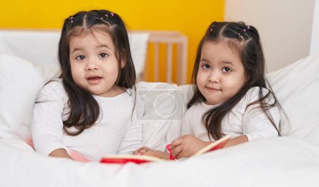 Téléchargez les photos : Adorable livre de lecture de filles jumelles couchées sur le lit dans la chambre - en image libre de droit