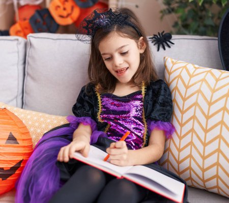 Téléchargez les photos : Adorable hispanique fille dessin sur ordinateur portable ayant fête d'Halloween à la maison - en image libre de droit