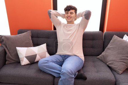 Photo for Non binary man relaxed with hands on head sitting on sofa at home - Royalty Free Image
