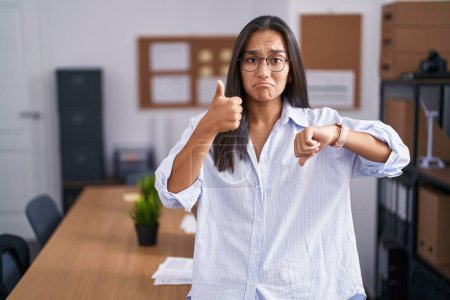 Photo for Young hispanic woman at the office doing thumbs up and down, disagreement and agreement expression. crazy conflict - Royalty Free Image
