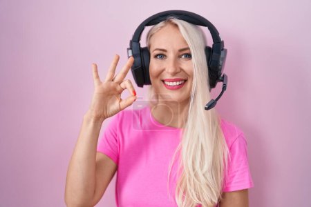 Téléchargez les photos : Femme caucasienne écoutant de la musique à l'aide d'écouteurs souriant positif faire ok signe avec la main et les doigts. expression réussie. - en image libre de droit