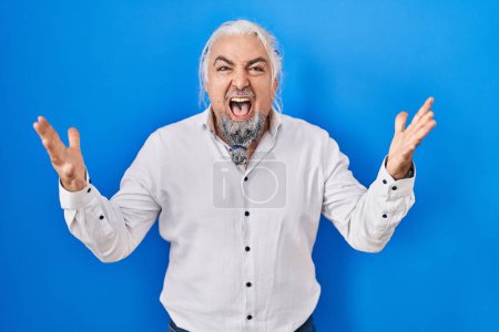 Photo for Middle age man with grey hair standing over blue background crazy and mad shouting and yelling with aggressive expression and arms raised. frustration concept. - Royalty Free Image