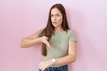 Photo for Beautiful brunette woman standing over pink background in hurry pointing to watch time, impatience, upset and angry for deadline delay - Royalty Free Image