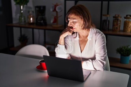 Foto de Mujer hispana de mediana edad usando laptop en casa por la noche cansada frotando nariz y ojos sintiendo fatiga y dolor de cabeza. concepto de estrés y frustración. - Imagen libre de derechos