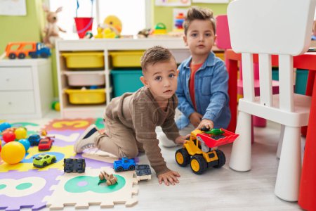 Adorable boys playing with tractor and dinosaur toy sitting on floor at kindergarten