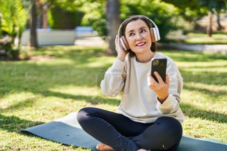 Téléchargez les photos : Femme d'âge moyen écoutant de la musique assise sur une herbe au parc - en image libre de droit