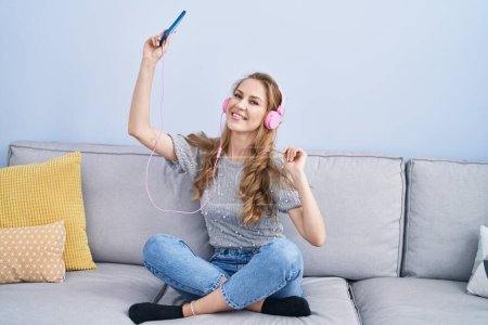 Photo for Young blonde woman listening to music and dancing at home - Royalty Free Image