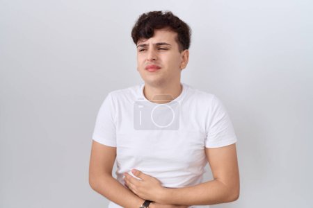 Photo for Young non binary man wearing casual white t shirt with hand on stomach because indigestion, painful illness feeling unwell. ache concept. - Royalty Free Image