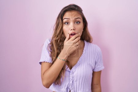 Photo for Young hispanic woman standing over pink background looking fascinated with disbelief, surprise and amazed expression with hands on chin - Royalty Free Image