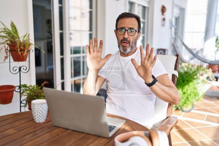 Photo for Middle age man using computer laptop at home moving away hands palms showing refusal and denial with afraid and disgusting expression. stop and forbidden. - Royalty Free Image