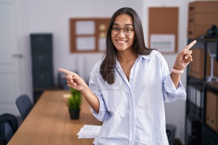 Téléchargez les photos : Jeune femme hispanique au bureau souriant confiant pointant avec les doigts vers différentes directions. espace de copie pour la publicité - en image libre de droit