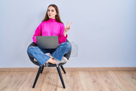 Photo for Young hispanic girl working using computer laptop smiling with happy face winking at the camera doing victory sign with fingers. number two. - Royalty Free Image