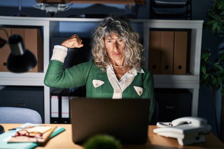 Foto de Mujer de mediana edad que trabaja por la noche usando computadora portátil fuerte persona que muestra el músculo del brazo, confiado y orgulloso de poder - Imagen libre de derechos