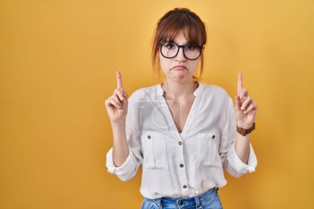 Photo for Young beautiful woman wearing casual shirt over yellow background pointing up looking sad and upset, indicating direction with fingers, unhappy and depressed. - Royalty Free Image