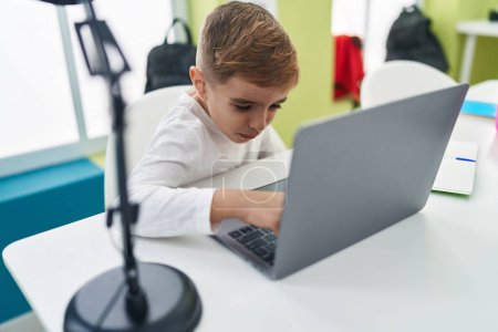 Téléchargez les photos : Adorable élève hispanique garçon en utilisant un ordinateur portable assis sur la table en classe - en image libre de droit