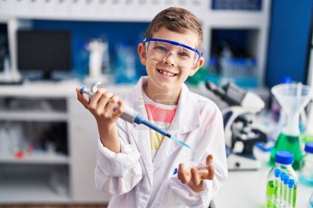 Foto de Niño rubio vistiendo uniforme científico usando pipeta en laboratorio - Imagen libre de derechos