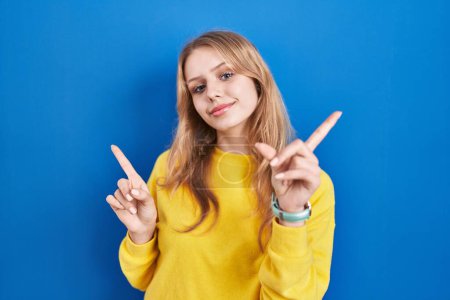 Téléchargez les photos : Jeune femme caucasienne debout sur fond bleu souriant confiant pointant avec les doigts vers différentes directions. espace de copie pour la publicité - en image libre de droit