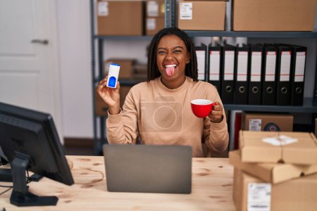 Photo for Young african american with braids working at small business ecommerce drinking a coffee with sweetener sticking tongue out happy with funny expression. - Royalty Free Image