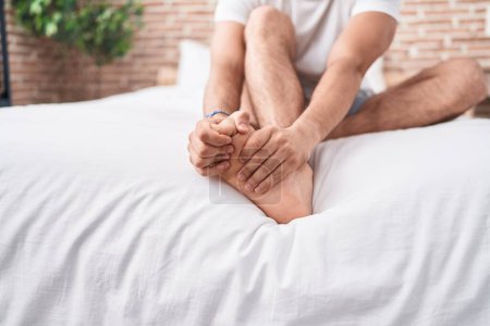 Foto de Joven hispano sufriendo por dolor de pies sentado en la cama en el dormitorio - Imagen libre de derechos