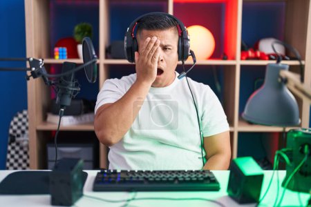 Photo for Young hispanic man playing video games yawning tired covering half face, eye and mouth with hand. face hurts in pain. - Royalty Free Image