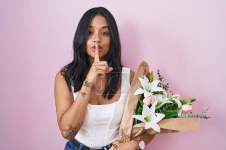 Téléchargez les photos : Femme brune tenant un bouquet de fleurs blanches demandant à se taire avec le doigt sur les lèvres. silence et concept secret. - en image libre de droit