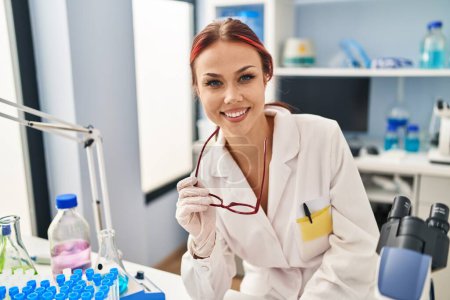 Photo for Young caucasian woman scientist smiling confident holding glasses at laboratory - Royalty Free Image