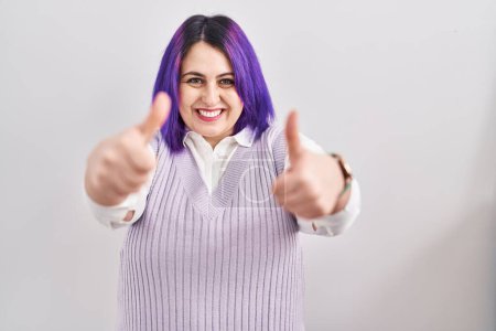 Téléchargez les photos : Plus taille femme avec les cheveux violets debout sur fond blanc approuvant faire un geste positif avec la main, pouces levés souriant et heureux pour le succès. geste gagnant. - en image libre de droit