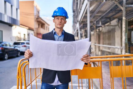 Photo for Young man architect standing with relaxed expression looking blueprint at street - Royalty Free Image