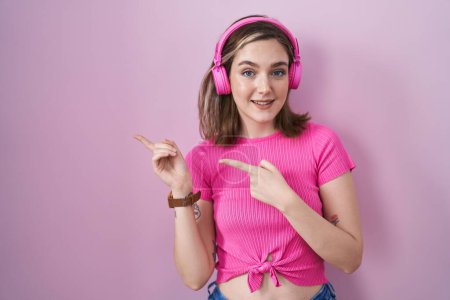 Photo for Blonde caucasian woman listening to music using headphones smiling and looking at the camera pointing with two hands and fingers to the side. - Royalty Free Image
