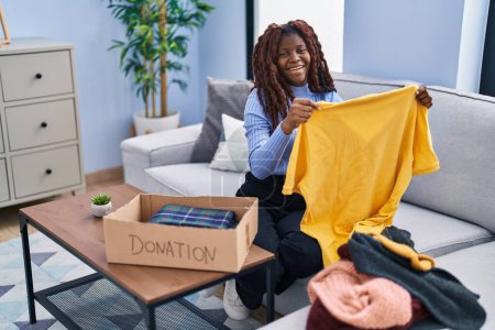 Téléchargez les photos : Afro-américaine femme souriante confiante mettre des vêtements sur les dons boîte de carton à la rue - en image libre de droit