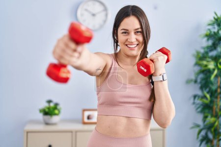 Téléchargez les photos : Jeune femme souriant entraînement confiant exercice de boxe à l'aide d'haltères à la maison - en image libre de droit