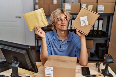 Téléchargez les photos : Jeune homme travaillant dans une petite entreprise e-commerce tenant des paquets souriant regardant vers le côté et regardant loin en pensant. - en image libre de droit
