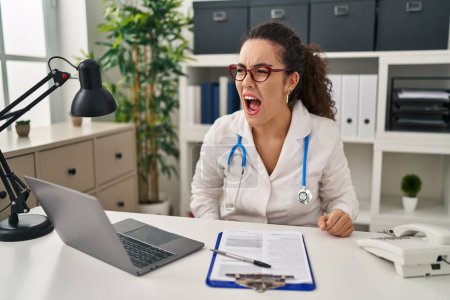 Photo for Young hispanic woman wearing doctor uniform and stethoscope angry and mad screaming frustrated and furious, shouting with anger. rage and aggressive concept. - Royalty Free Image