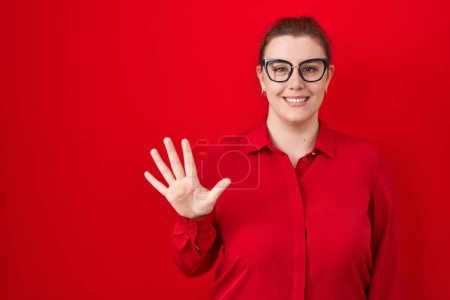 Photo for Young hispanic woman with red hair standing over red background showing and pointing up with fingers number five while smiling confident and happy. - Royalty Free Image