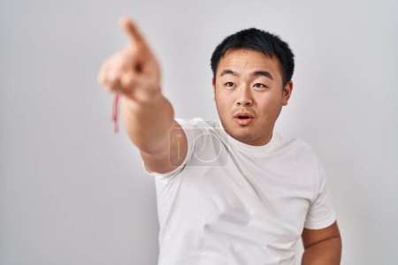 Photo for Young chinese man standing over white background pointing with finger surprised ahead, open mouth amazed expression, something on the front - Royalty Free Image