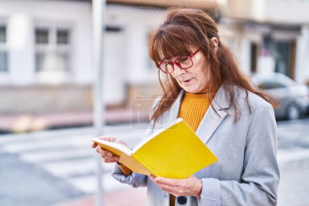 Téléchargez les photos : Femme d'âge moyen dirigeant d'entreprise lecture livre à la rue - en image libre de droit