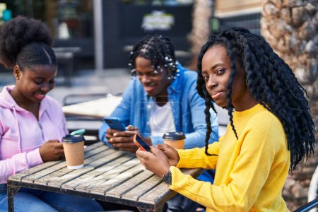 Téléchargez les photos : Des amis afro-américains utilisant un smartphone buvant du café assis sur un banc sur la terrasse du café - en image libre de droit