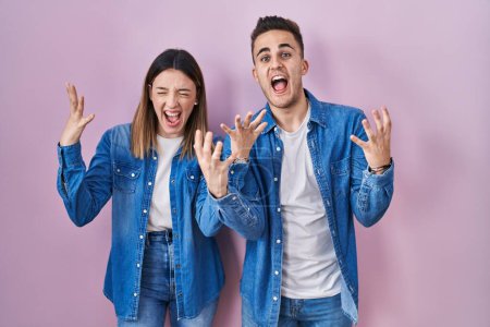 Photo for Young hispanic couple standing over pink background crazy and mad shouting and yelling with aggressive expression and arms raised. frustration concept. - Royalty Free Image
