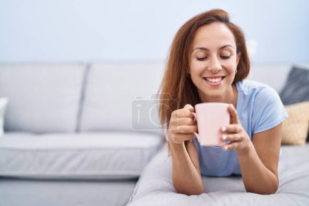 Téléchargez les photos : Jeune femme buvant du café couché sur le canapé à la maison - en image libre de droit