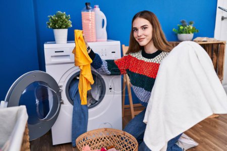 Foto de Mujer joven sonriendo confiada lavando ropa en la lavandería - Imagen libre de derechos