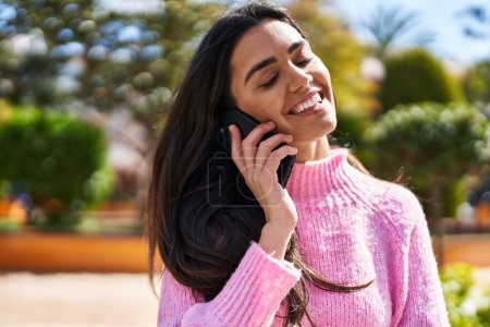 Téléchargez les photos : Jeune femme hispanique souriant confiant parler sur le smartphone au parc - en image libre de droit