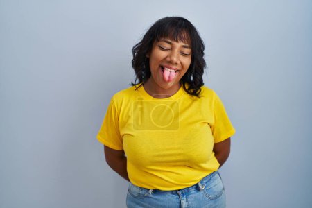 Photo for Hispanic woman standing over blue background sticking tongue out happy with funny expression. emotion concept. - Royalty Free Image