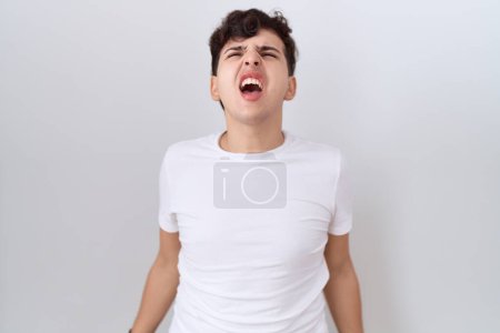 Téléchargez les photos : Jeune homme non binaire portant un t-shirt blanc décontracté en colère et fou criant frustré et furieux, criant de colère. rage et concept agressif. - en image libre de droit