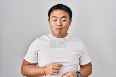 Téléchargez les photos : Jeune homme chinois debout sur fond blanc regardant la caméra souffler un baiser sur l'air étant belle et sexy. expression d'amour. - en image libre de droit