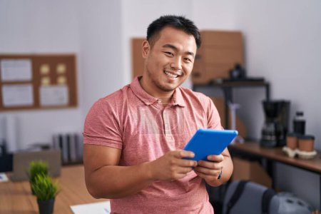 Téléchargez les photos : Jeune homme d'affaires chinois travailleur souriant confiant en utilisant le pavé tactile au bureau - en image libre de droit