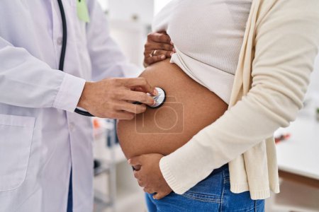 Téléchargez les photos : Jeune couple latin médecin et patient auscultant bébé à la clinique - en image libre de droit