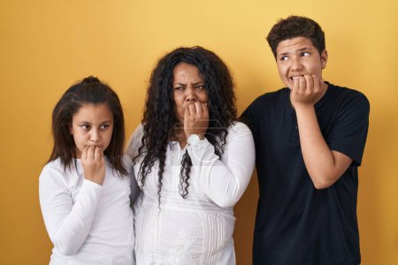 Photo for Family of mother, daughter and son standing over yellow background looking stressed and nervous with hands on mouth biting nails. anxiety problem. - Royalty Free Image