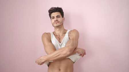 Téléchargez les photos : Jeune homme hispanique décoller t-shirt sur fond rose isolé - en image libre de droit